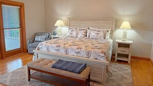 A bedroom with a bed, two bedside tables with lamps, a chair, a bench, and a window with blinds. - Serendipity on the Sound - Beautiful 4 BR Soundfront Home With Amenities Galore (Southern Shores)