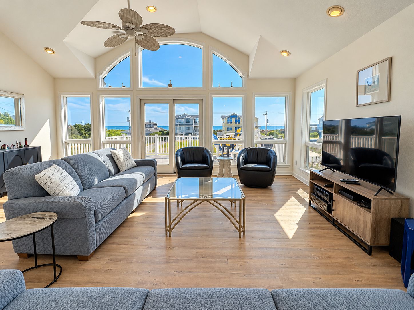 A spacious living room with a large window, a ceiling fan, a sofa, a coffee table, and a television.