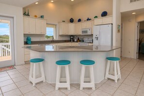 A kitchen with white cabinets, a central island with stools, a microwave, and a refrigerator.
