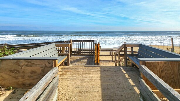 A wooden boardwalk leading to a beach with a wooden bench and a sign indicating a short distance to the beach.