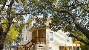 A two-story house with a wooden staircase, a porch, and a small outdoor seating area.