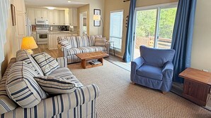 A living room with striped sofas, a coffee table, a blue armchair, and a kitchen in the background.