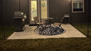 A covered patio area with a grill, table, chairs, and string lights.