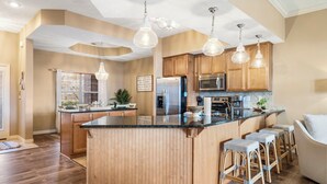 Una cocina moderna con armarios de madera, una isla central, taburetes de bar e iluminación colgante.