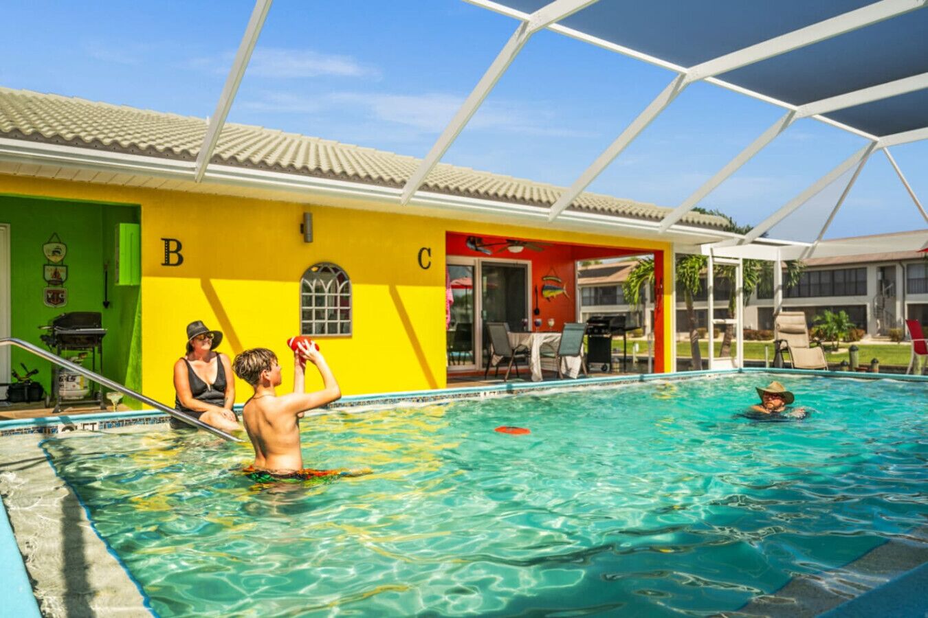A swimming pool with a covered area, a green wall with letters 'B' and 'C', and a person in the pool.