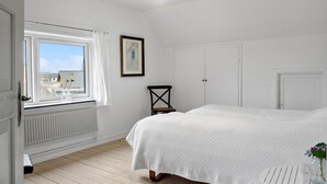 A bedroom with a bed, a radiator, a window with curtains, a chair, and a door. - Cozy home in Thyborøn with WiFi (Thyborøn)