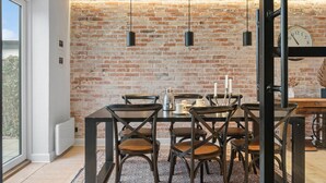 A dining area with a brick wall, a wooden table, and six chairs. - Cozy home in Thyborøn with WiFi (Thyborøn)