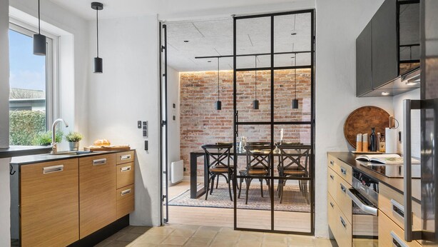 A modern kitchen with a brick wall, wooden cabinets, and a dining area with a table and chairs. - Cozy home in Thyborøn with WiFi (Thyborøn)