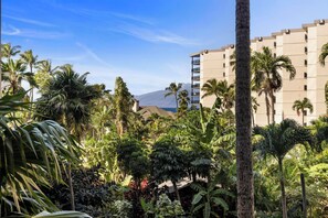 Un hotel con jardín tropical, palmeras y una montaña al fondo.