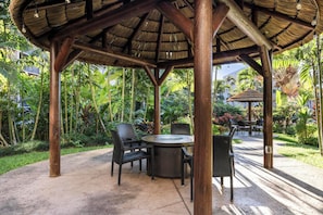 Relax in a serene outdoor space surrounded by lush tropical vegetation and a wooden pergola.