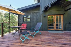 Um deck de madeira com uma mesa e cadeiras, uma cadeira vermelha e um grande guarda-sol.