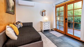 A bedroom with a bed, a nightstand, a mirror, and a large sliding glass door to a deck. - Meadow View Nest - Charming Studio in Oakhurst [Sleeps 3] (Oakhurst)