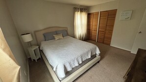 Un dormitorio con cama, mesita de noche, lámpara, ventana con cortinas y armario.