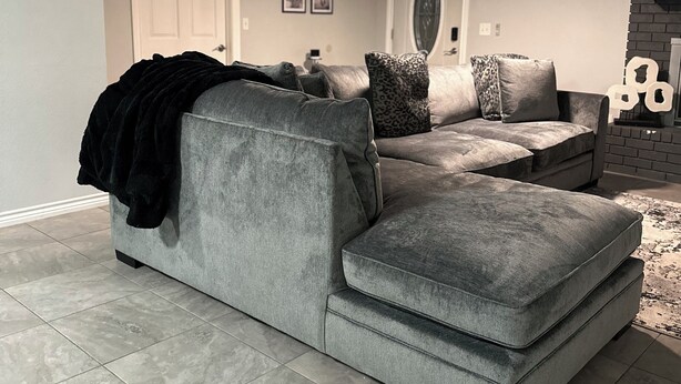 Un salón con un sofá seccional gris, un ventilador de techo y una chimenea.