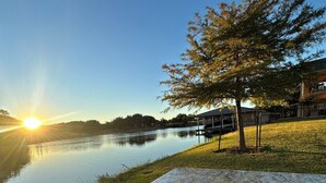Vista de un lago con un banco, un árbol y un edificio al fondo.