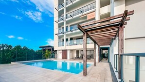 A modern building with a swimming pool, outdoor seating, and a covered area.