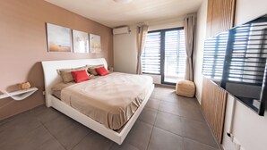 A modern bedroom with a large bed, a flat-screen TV, and a window with blinds.