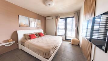 A modern bedroom with a large bed, a flat-screen TV, and a window with blinds.