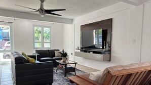 Una sala de estar moderna con un sofá negro, un banco de madera, una mesa de centro y un televisor montado en la pared.