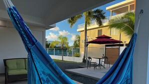 Una hamaca en un espacio exterior cubierto con patio, sillas y un paraguas rojo.