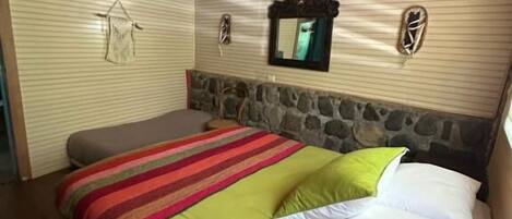 Un dormitorio con techo de madera, pared de acento de piedra, cama con colcha a rayas y un espejo.