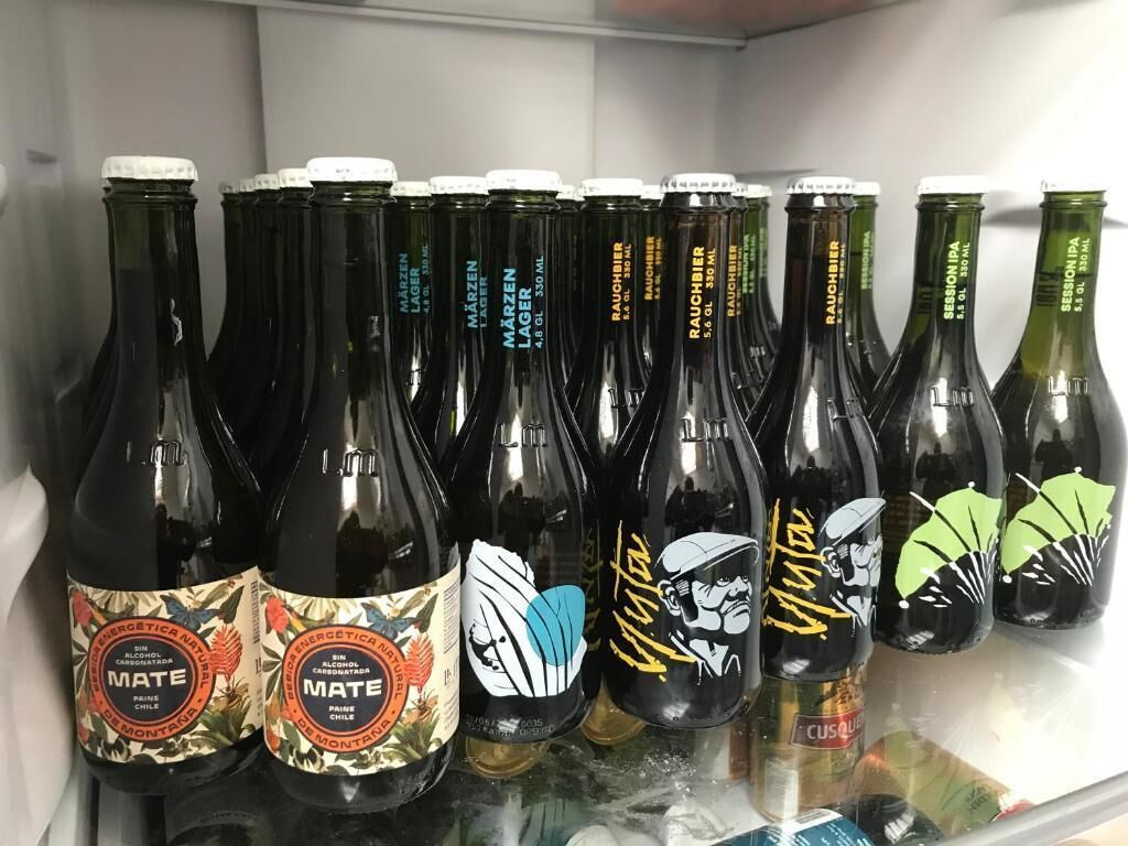 Een koelkast gevuld met verschillende flessen bier, waaronder merken zoals 'MATE' en 'Raubier'.