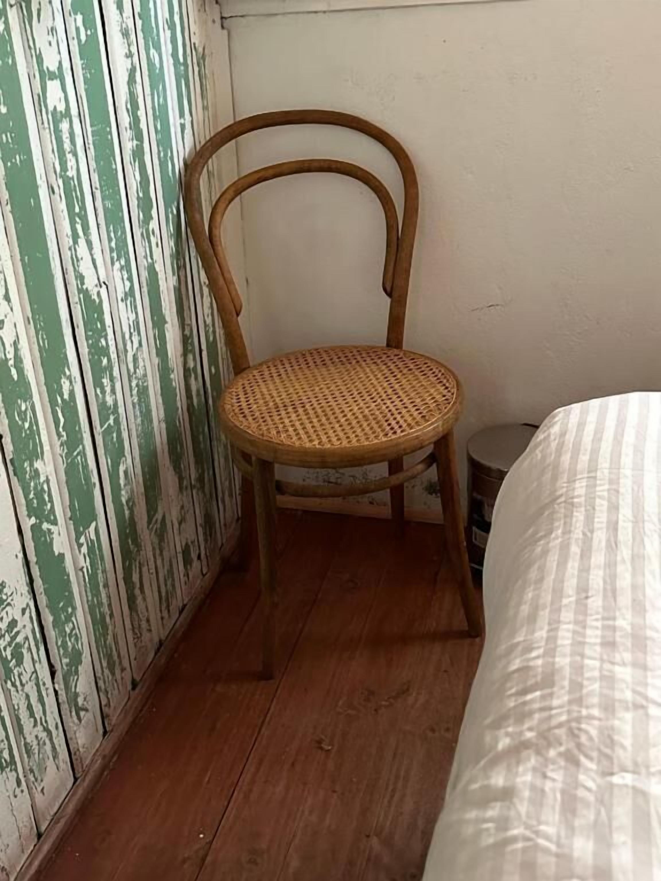 Ein kleiner Raum mit einem Holzstuhl, einem Bett mit gestreifter Bettdecke und einer grün-weißen Wand.