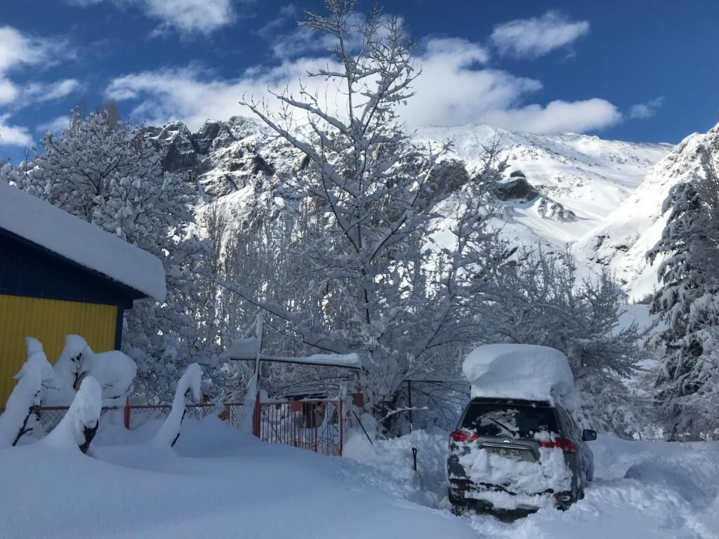 Paisaje montañoso cubierto de nieve con un automóvil estacionado y un edificio con techo amarillo.