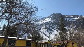 Un bâtiment jaune aux fenêtres et aux portes bleues, entouré de neige et d’arbres, avec une montagne en arrière-plan.