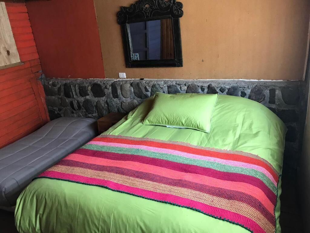 A bed with a green and pink striped blanket, a green pillow, and a grey pillow.