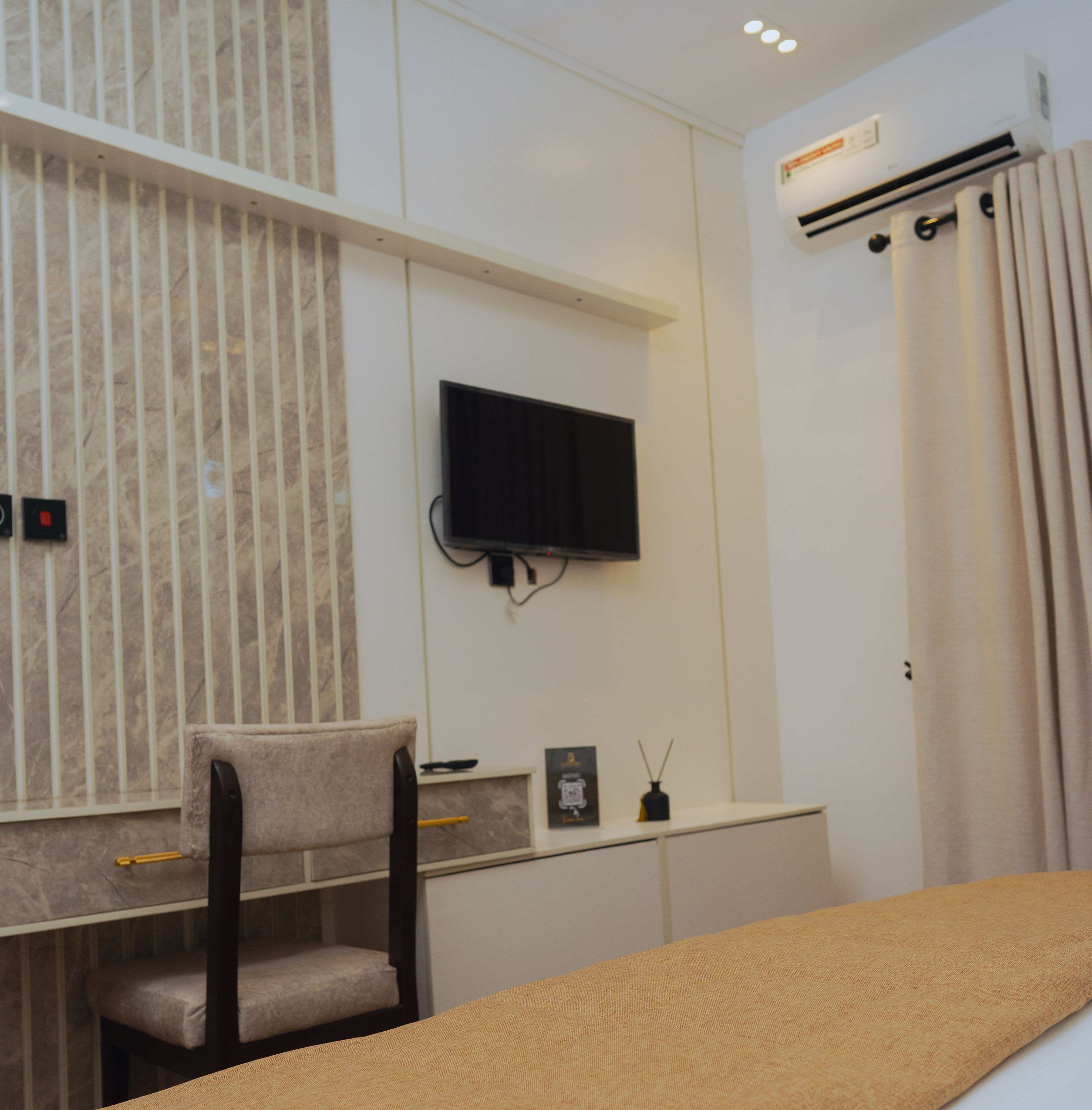 Un dormitorio moderno con cama, escritorio, silla, televisión y aire acondicionado.