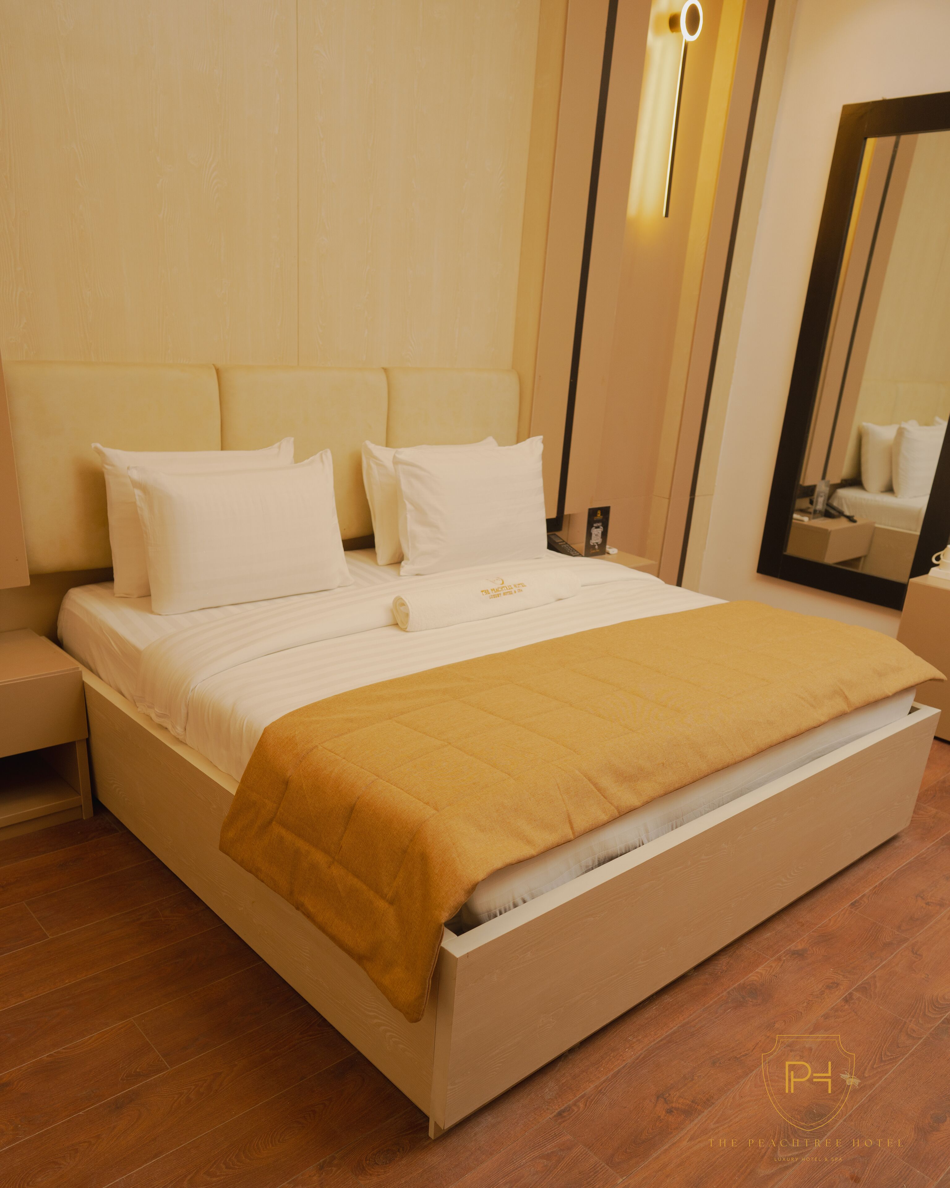 A bed with a white headboard, a mustard-colored blanket, and a wooden floor.