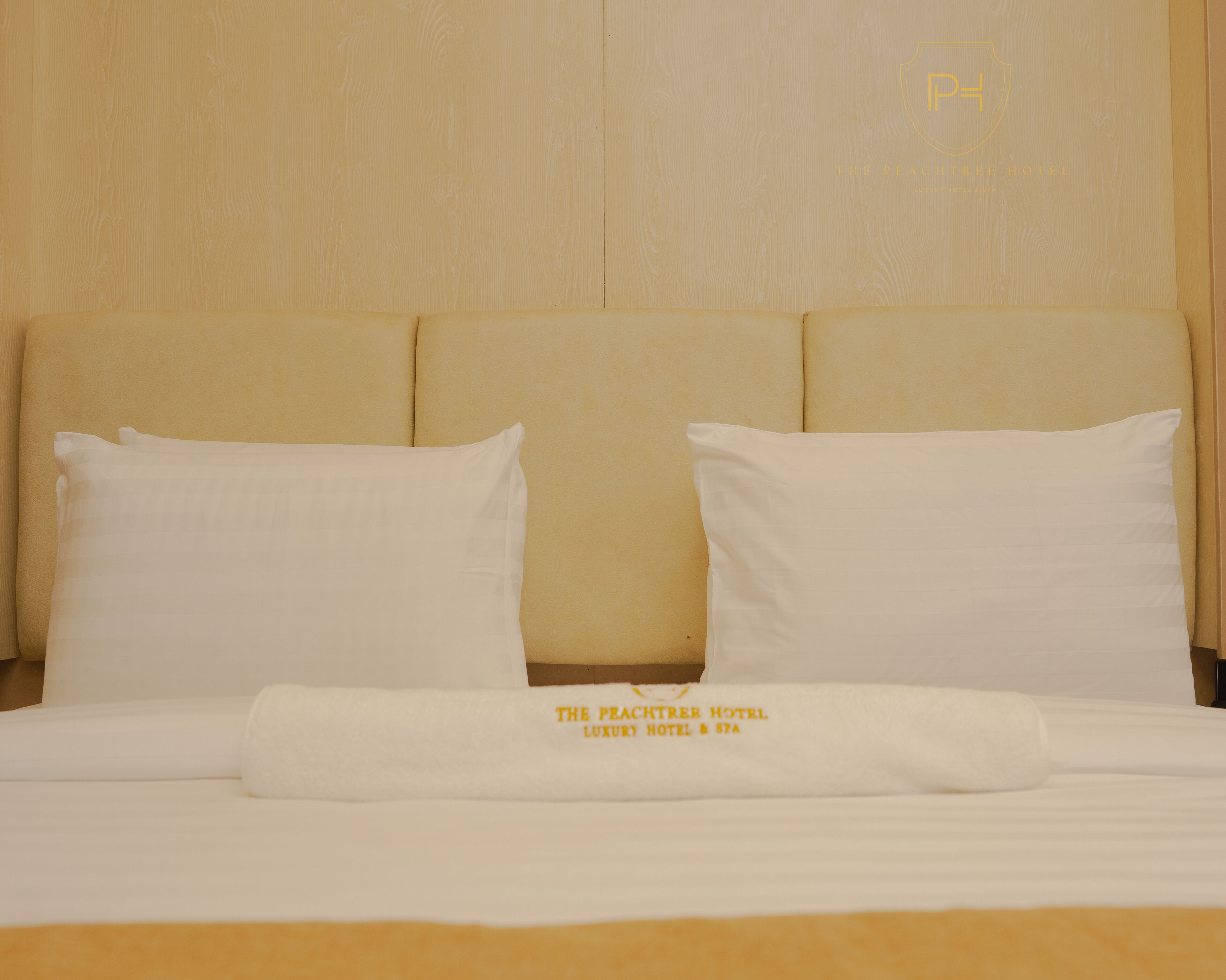 A neatly made bed with white linens and pillows, a headboard, and a visible logo on the headboard.