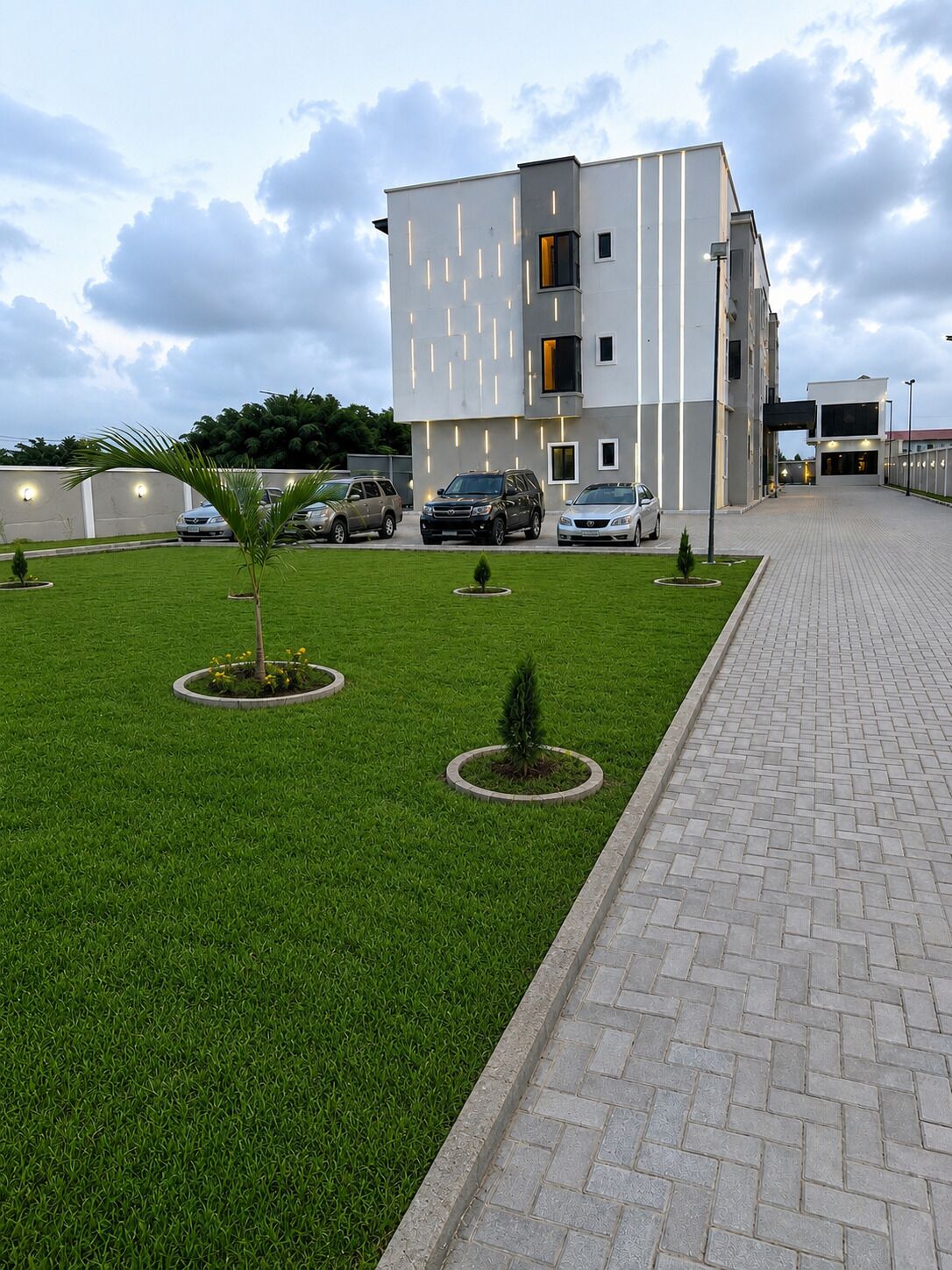 A modern building with a paved walkway, a well-maintained lawn, and several parked cars.