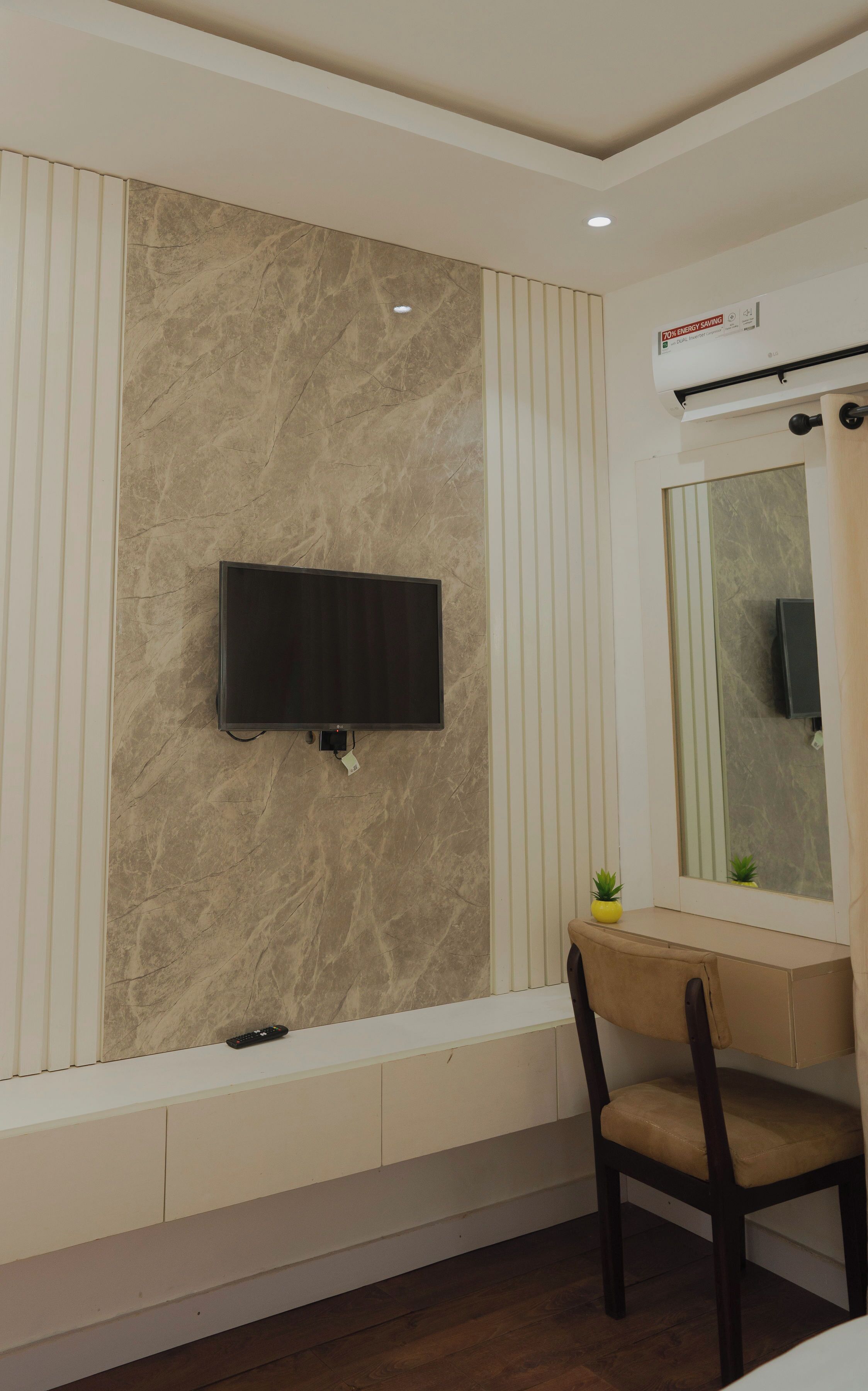 Un baño moderno con pared de mármol, un televisor montado, un tocador con espejo y una silla.