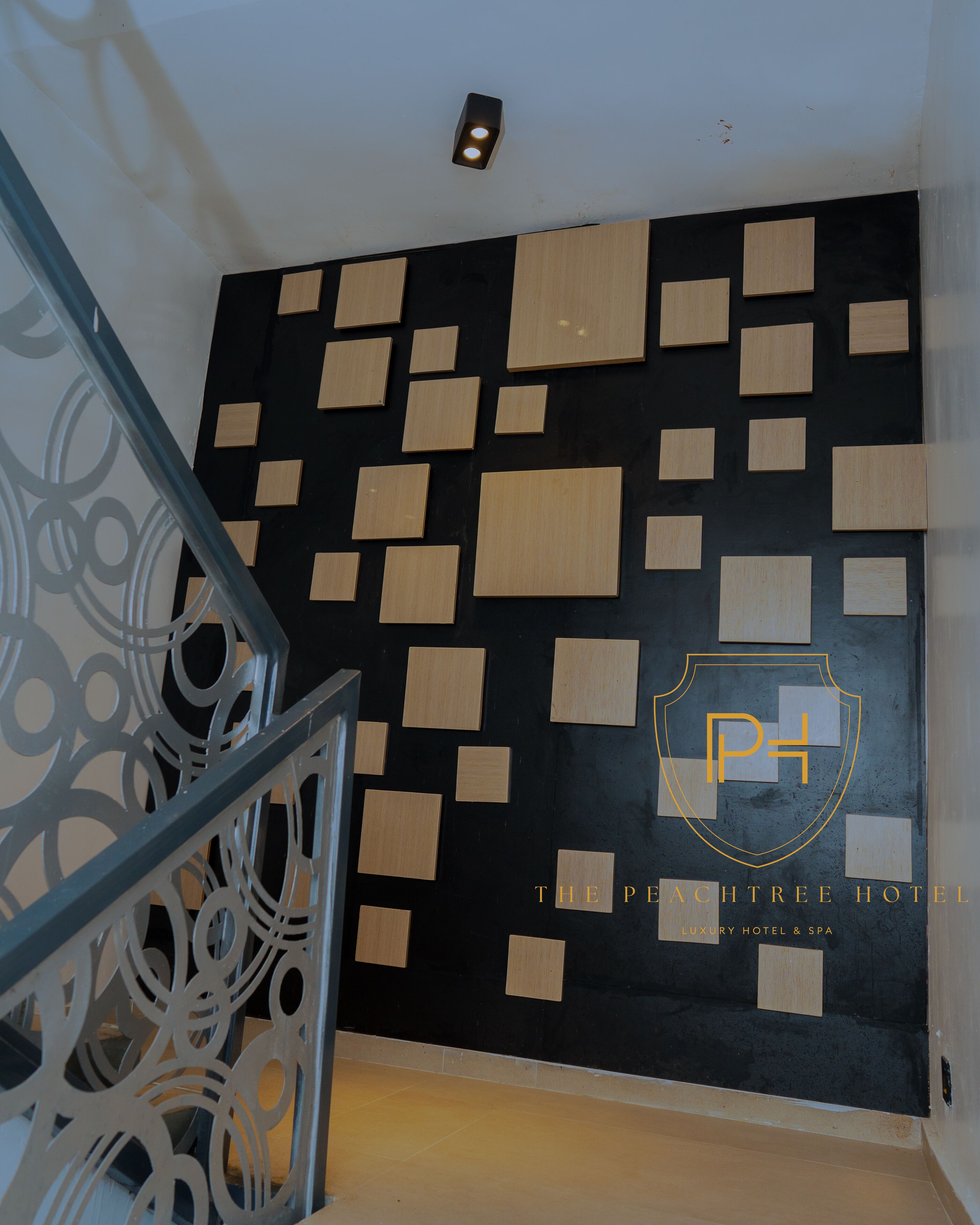A modern interior with a black and wood panel wall, a metal railing, and a logo for The Peachtree Hotel.