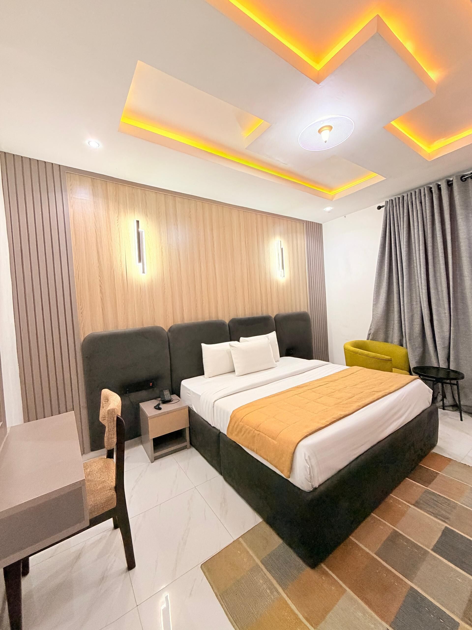 A modern hotel room with a bed, bedside tables, a desk, and a chair.