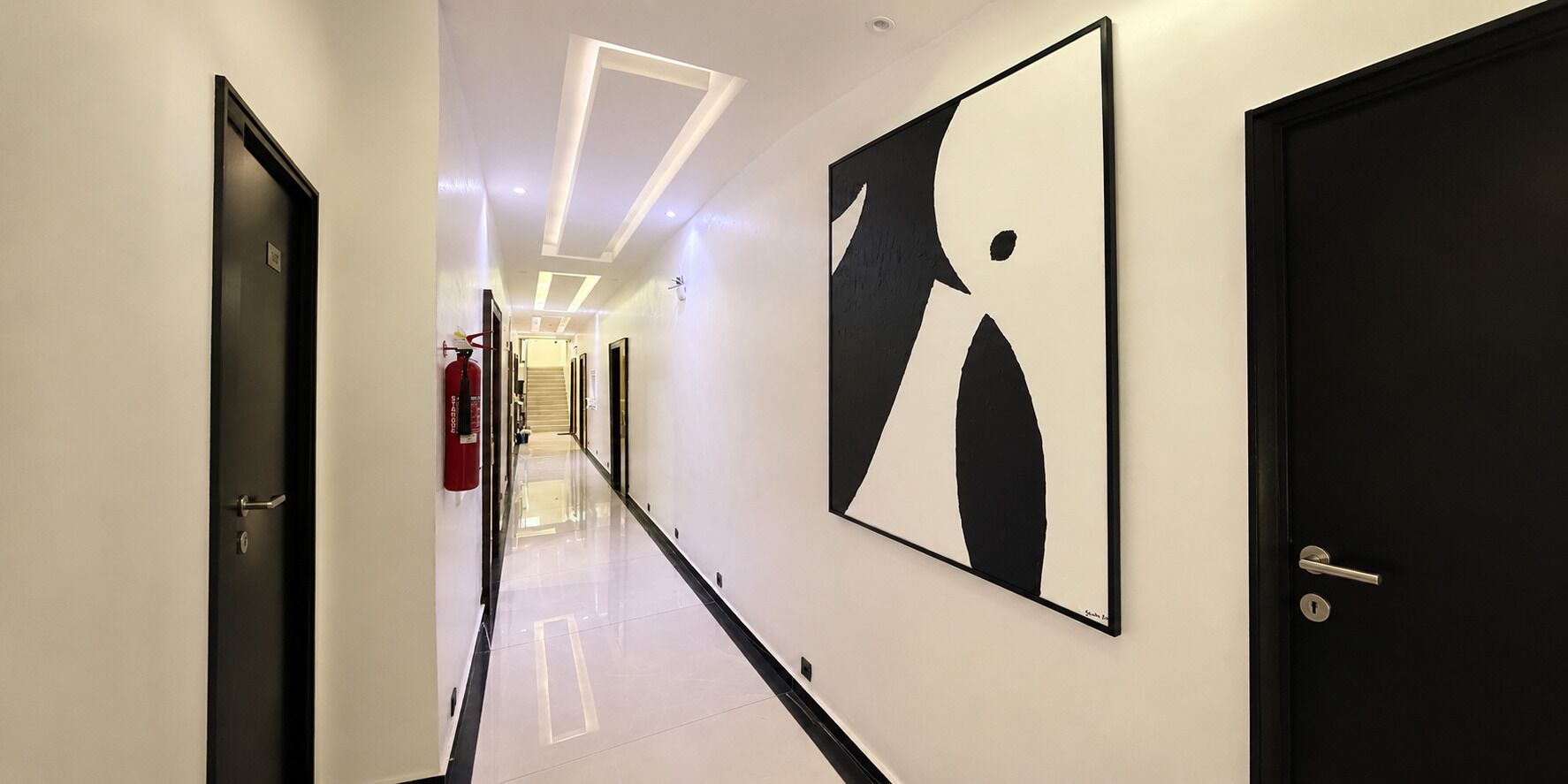 A hallway with a black and white abstract painting, a fire extinguisher, and a door with a handle.