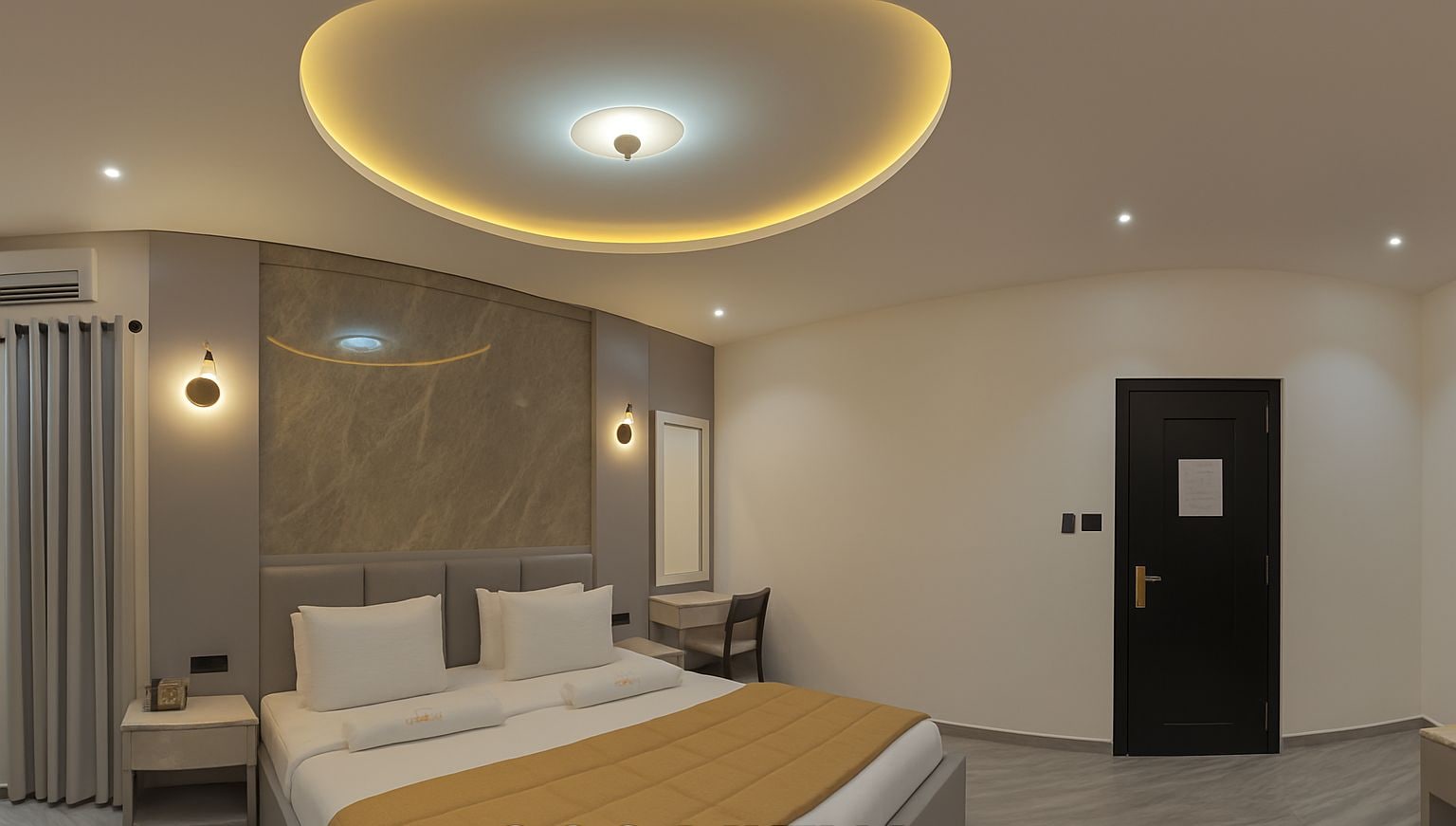A modern hotel room with a large bed, a round ceiling light, a mirror, and a door.