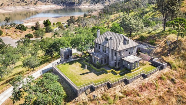 A large, historic house with a spacious lawn, a small tower, and a view of a lake.