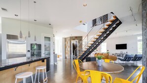 A modern kitchen with a central island, bar stools, and a dining area with yellow chairs.