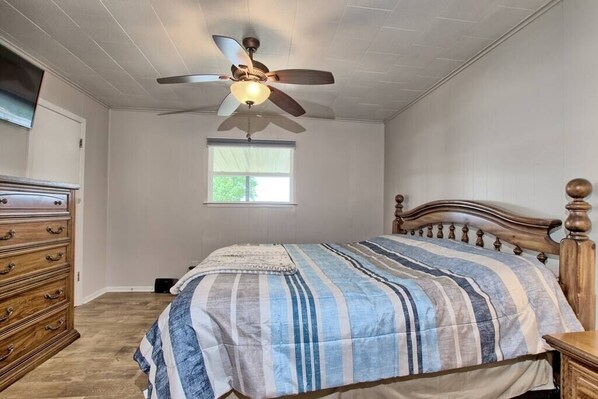 A bedroom with a bed, wooden dresser, ceiling fan, and a window. - Lakefront Home -Private Dock, Fishing and Stunning Views (Milam)