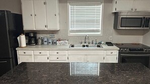 A kitchen with a central island, two bar stools, a microwave, a stove, and a window with blinds. - Lakefront Home -Private Dock, Fishing and Stunning Views (Milam)