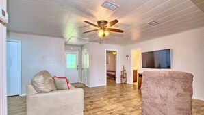 A spacious living room with a ceiling fan, a large TV, and a plush armchair. - Lakefront Home -Private Dock, Fishing and Stunning Views (Milam)