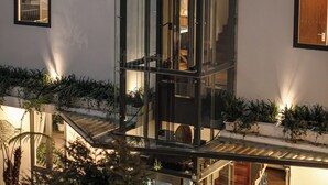 Un edificio moderno con un hueco de ascensor de vidrio, una escalera de madera y obras de arte enmarcadas en las paredes.