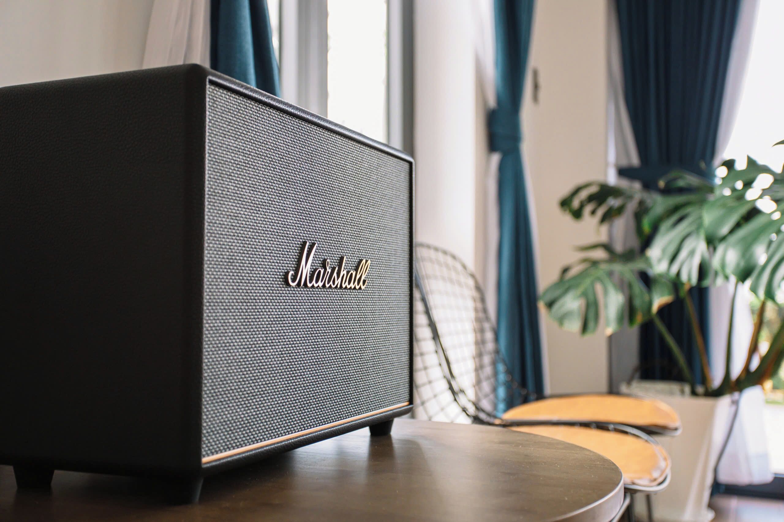 Een Marshall speaker op een houten tafel in een kamer met een stoel en een potplant.
