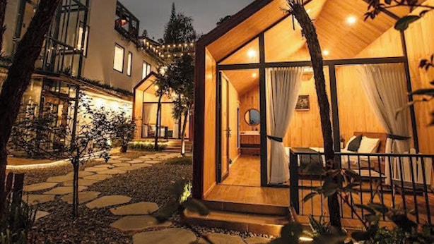 Un acogedor edificio de estilo cabaña con fachada de madera y ventanas amplias, rodeado de un sendero de piedra y vegetación.