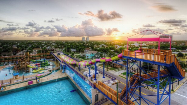 A water park with a large pool, slides, and a high platform with stairs.