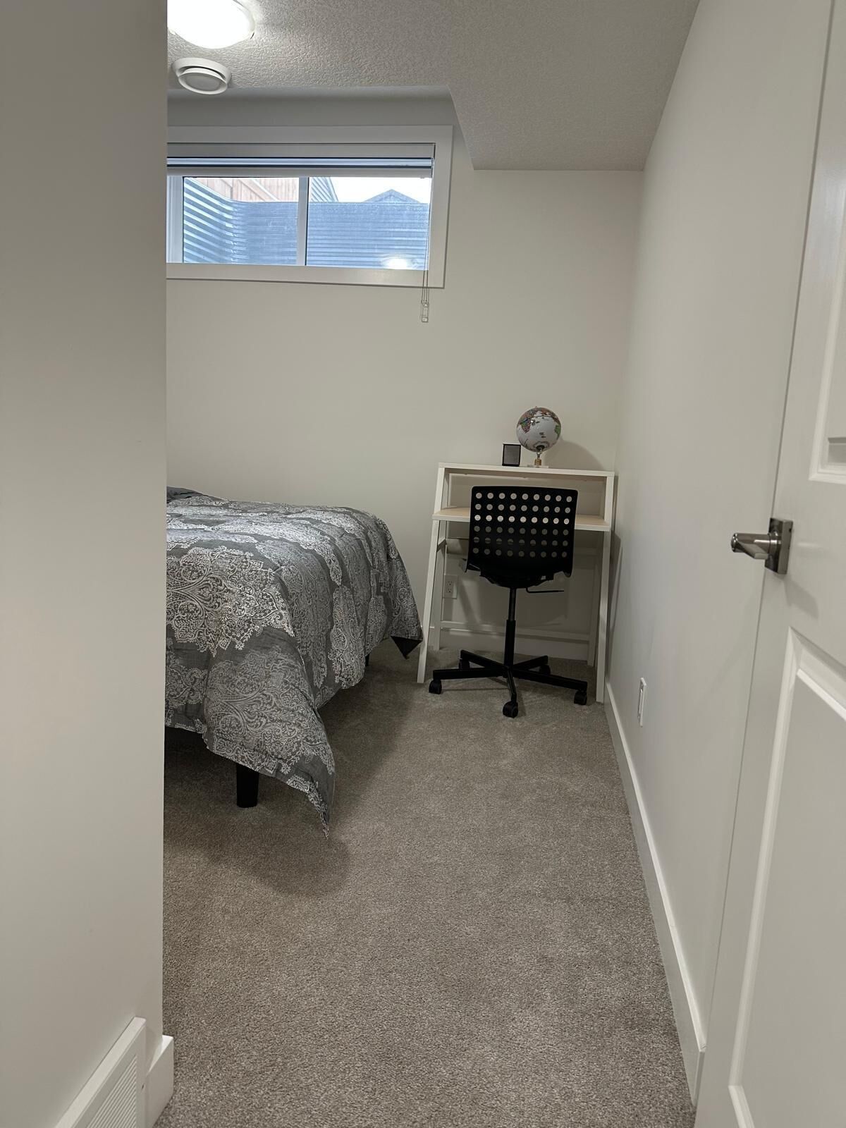Ein Schlafzimmer mit Bett, Schreibtisch, Stuhl, Globus und einem Fenster mit Jalousien.