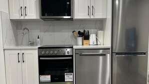 A modern kitchen with white cabinets, stainless steel appliances, a microwave, oven, dishwasher, and a refrigerator. - Luxury 2 Bedroom Basement Suite in NW, Calgary (Calgary)